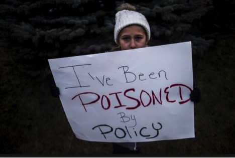Person holding sign that reads I've been poisoned by policy